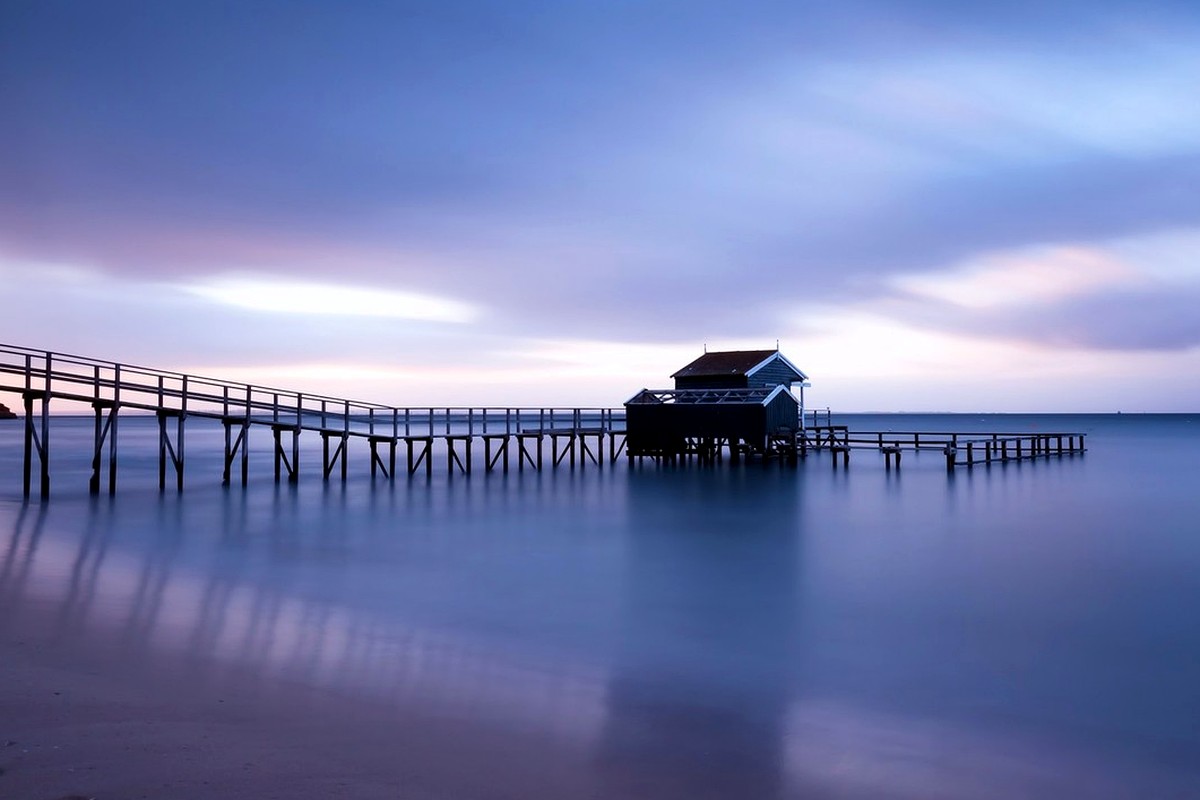 A long pier over calm water beneath a blue and violet evening sky.