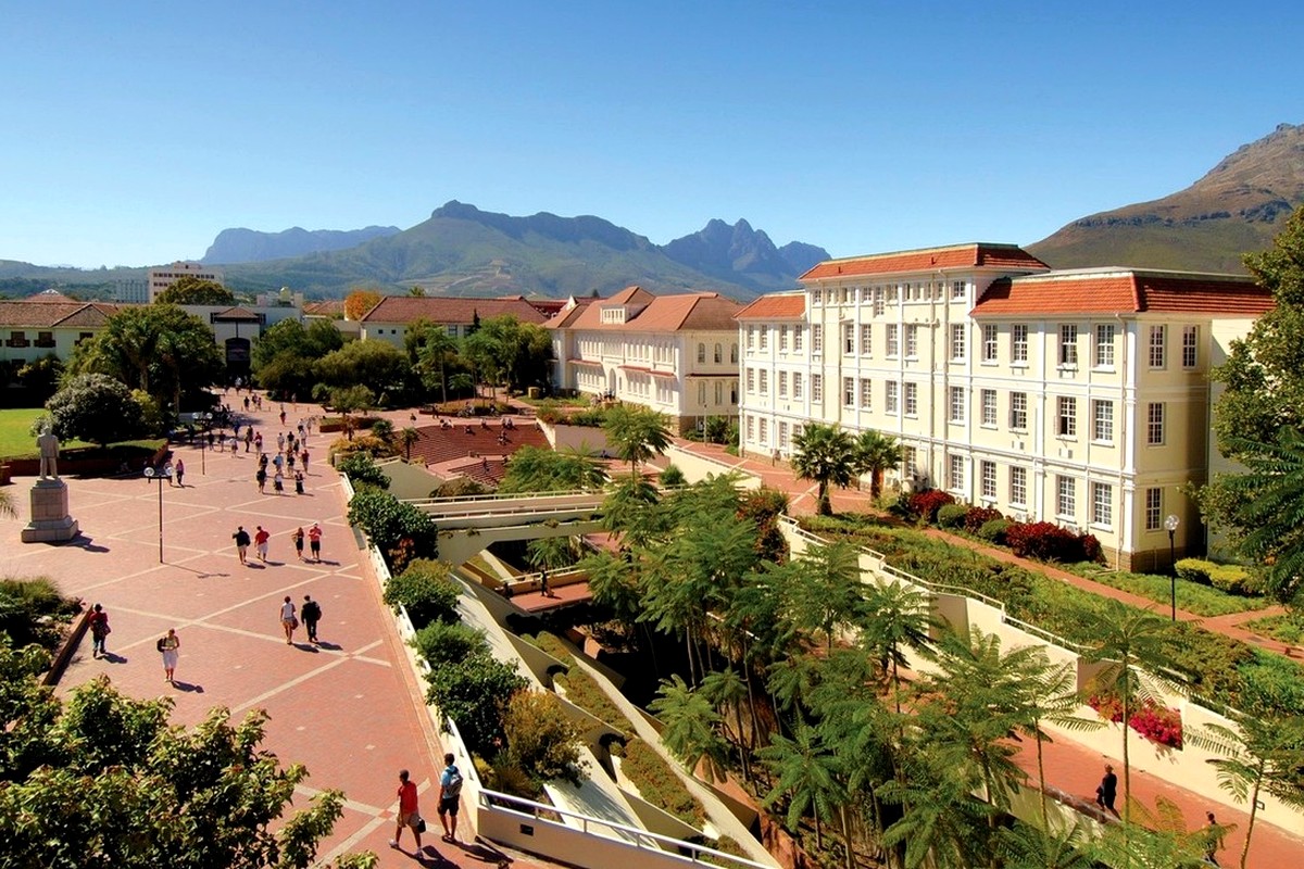 A landscaped campus garden with paths, trees, buildings, and mountains in clear daylight.